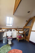 Toilet with a wooden seat and lid and a sink with a wooden washstand in an attic bathroom