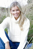 Junge blonde Frau in weißem Rollkragenpullover und Jeans in der Natur