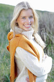 Young blond woman in white turtleneck sweater, with yellow knitted sweater slung over shoulders in nature