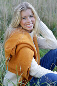 Young blond woman in white turtleneck sweater, with yellow knitted sweater slung over shoulders in nature