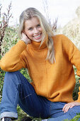 Junge blonde Frau in gelbem Rollkragenpullover und Jeans in der Natur