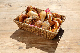 Various freshly baked goods in a basket on a wooden table (rolls and pretzels)