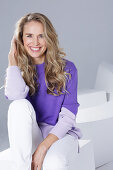 Blond woman wearing a purple sweater and white trousers