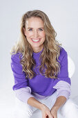 Blond woman wearing a purple sweater and white trousers