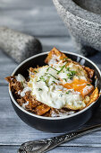 From above closeup traditional Mexican breakfast dish called chilaquiles with beef cheek mole served in bowl with fried egg and Oaxaca cheese