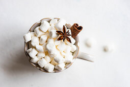 Cup of hot chocolate and mini marshmallow with cinnamon stock and anise star on white concrete background