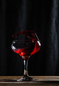 Splashing tasty alcoholic red wine with small drops in transparent wineglass placed on table against black background