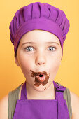 Lustiges Mädchen in lila Kochkleidung mit schokoladenverschmiertem Mund