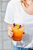 Orangefarbener Sommercocktail, garniert mit essbaren Blüten