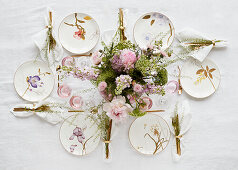 Plates with floral motifs, gold-coloured cutlery and bouquet of flowers on a festively laid table