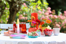 Tisch mit farbenfrohen Vasen, Blumen, Getränken und Kerzen im Garten