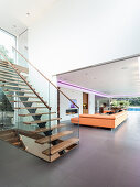 Treppe mit Glasbalustrade in offenem Wohnraum, im Hintergrund Sofalandschaft