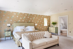 Double bed with high headboard in front of wallpapered wall and light sofa in bedroom