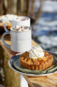 Apfeltartelett mit Sahne serviert mit einer Tasse Kakao im winterlichen Garten