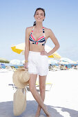 Young brunette woman in a striped bikini top and white shorts on the beach