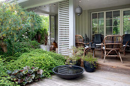 Wooden veranda with seating furniture, in the foreground wooden deck, and dense planting