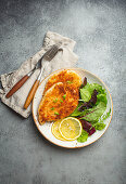 Crispy panko breaded fried chicken fillet with green salad and lemon