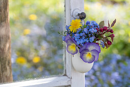 Small bouquet in eggshell with dandelions; ornamental apple; forget-me-nots and horned violets hung on an old window.