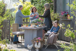 Gedeckter Tisch mit Osterdekoration, Frauen stoßen mit Sekt an, auf der Terrasse