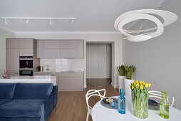 Open living room with round white table and blue sofa, built-in kitchen in the background