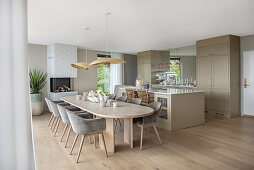 Long dining table in light wood with elegant, upholstered shell chairs in open-plan living room