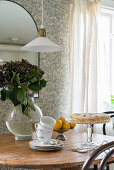 Tea cups and saucers with cake and glass vase with flowers on wooden table