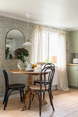 Round wooden table with Thonet chairs in front of wallpapered wall with mirror