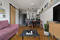 Open-plan living room with lilac-colored sofa, coffee table and TV cabinet