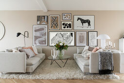 Light sofas, glass table and pictures on beige-colored wall in open-plan living room