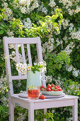 Frische Erdbeeren, Getränk und Blütenstrauß auf Holzstuhl im Garten
