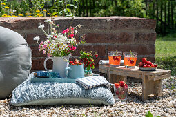 Blumenstrauß und Krug mit Erdbeeren auf Bodenkissen im Garten daneben Bänkchen mit Getränken