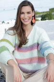 Young woman in light-coloured knitted jumper with coloured stripes and beige trousers