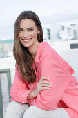 Young woman in salmon coloured shirt with pearl necklace and light coloured trousers