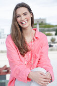 Young woman in salmon coloured shirt with pearl necklace and light coloured trousers