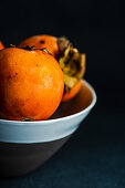 Ripe persimmon fruits in the bowl on stone background