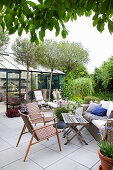 Comfortable seating area on the terrace made with concrete slabs, with globe cherry trees and greenhouse in the background