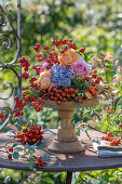 Herbstliches Blumenarrangement mit Rosen, Hortensien und Hagebutten auf Holzständer