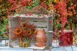 Autumn bouquet of sunflowers and rose hip twigs in wooden box, next to it clay pots and watering can