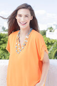 A cheerful young woman wearing an orange summer blouse with a necklace