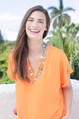 A cheerful young woman wearing an orange summer blouse with a necklace