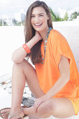 A cheerful young woman wearing an orange summer blouse with a necklace