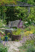Wasserbrunnen im sommerlichen Garten, dahinter Gartenplatz mit Pergola und Holzbank