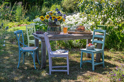 Sommerlicher Blumenstrauß mit Sonnenblumen, Kugeldisteln, großer Bibernelle, Bienenfreund, Oregano und Kosmeen auf Holztisch im Garten