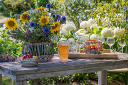 Sommerlicher Blumenstrauß mit Sonnenblumen, Kugeldisteln, großer Bibernelle, Bienenfreund, Oregano und Kosmeen auf Holztisch im Garten