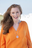 Young, blonde woman in an orange blouse, in a good mood, on the beach