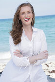 Good-humoured young, blond woman in white blouse dress by the sea