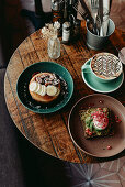 Avocado toasted topped with an egg, pancakes topped with banana and nuts, and a latte on breakfast table