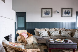Sofa mit Kissen und Korbsessel mit Schaffell im Wohnraum mit halbhoher Holzverkleidung