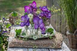 Purple gladiolus blossoms and maidenhair in glass vases on tray