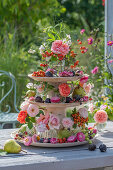 Etagere mit Rosenblüten, Strohblumen, Duftwicken, Hagebutten und Herbstfrüchten als Tischdekoration